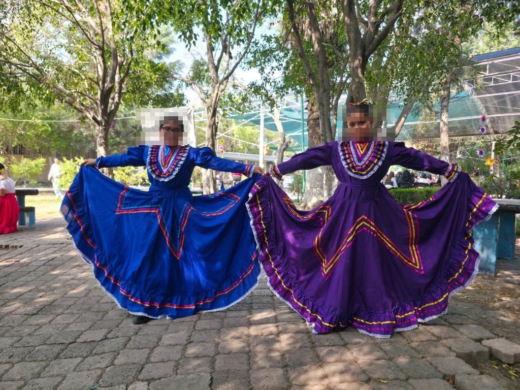 Dos alumnas con vestidos de Jalisco azul y morado posando con la falda extendida