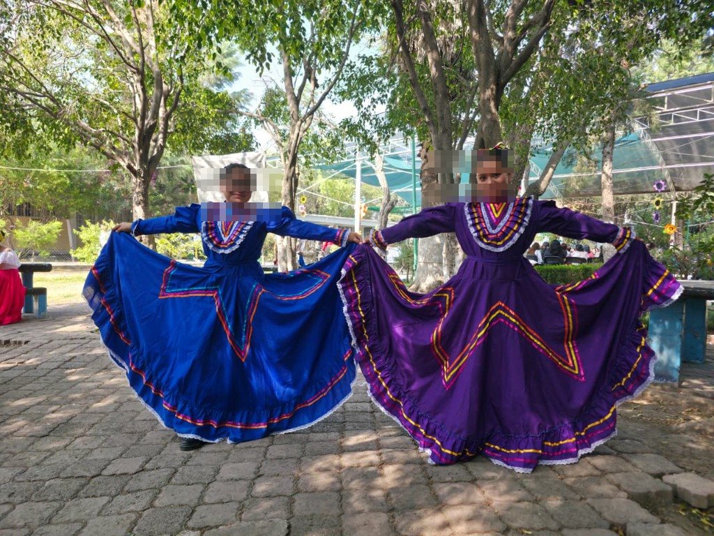 Dos alumnas con trajes de Jalisco bailando en el patio entre los árboles