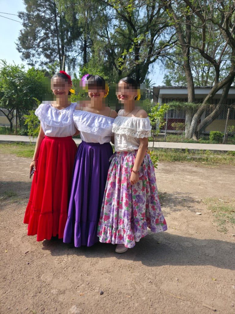 Tres alumnas con blusas blancas y faldas largas de colores antes de su presentación