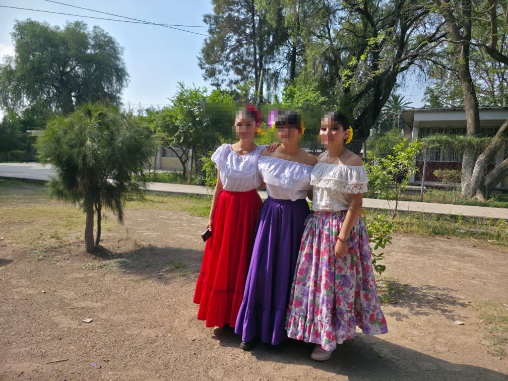 Tres alumnas en traje regional posando bajo los árboles del patio escolar